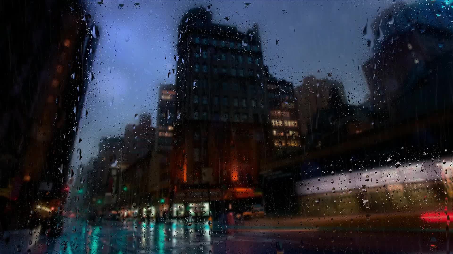 A city street at night in the rain, its lights blurred on the wet road