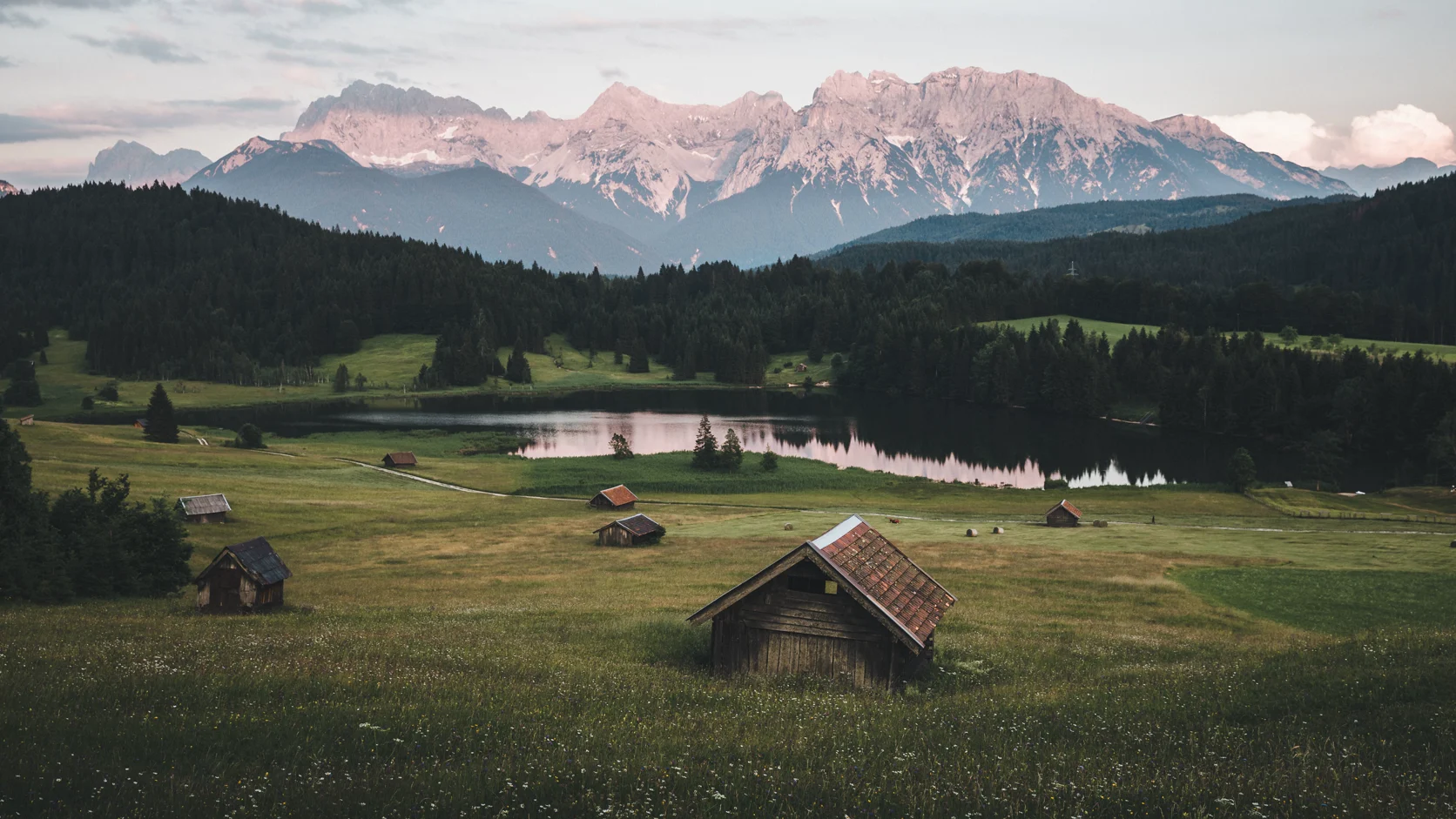 A wooden hut on an alpine meadow by a lake, mountains behind