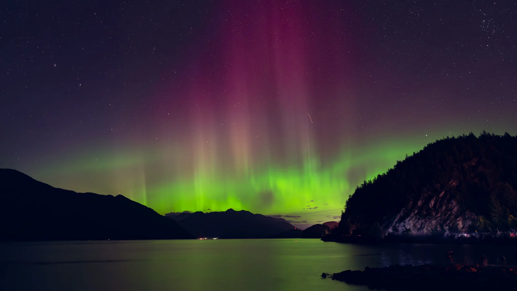 The northern lights, green and pink, over a still mountain lake